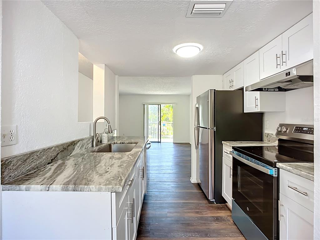 A galley kitchen features white cabinets, granite countertops, stainless steel appliances, and wood-look flooring — 5310 26TH STREET W UNIT 306, BRADENTON, FL
