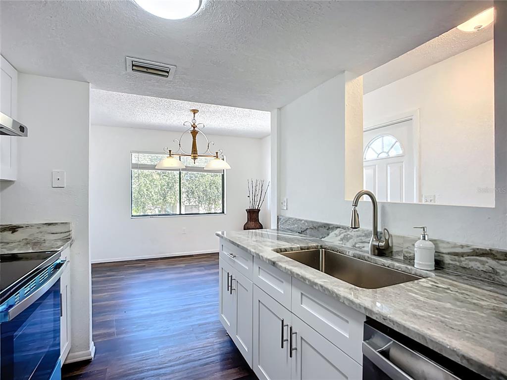 A kitchen with white cabinets and marble-look countertops overlooks a dining area with wood flooring — 5310 26TH STREET W UNIT 306, BRADENTON, FL