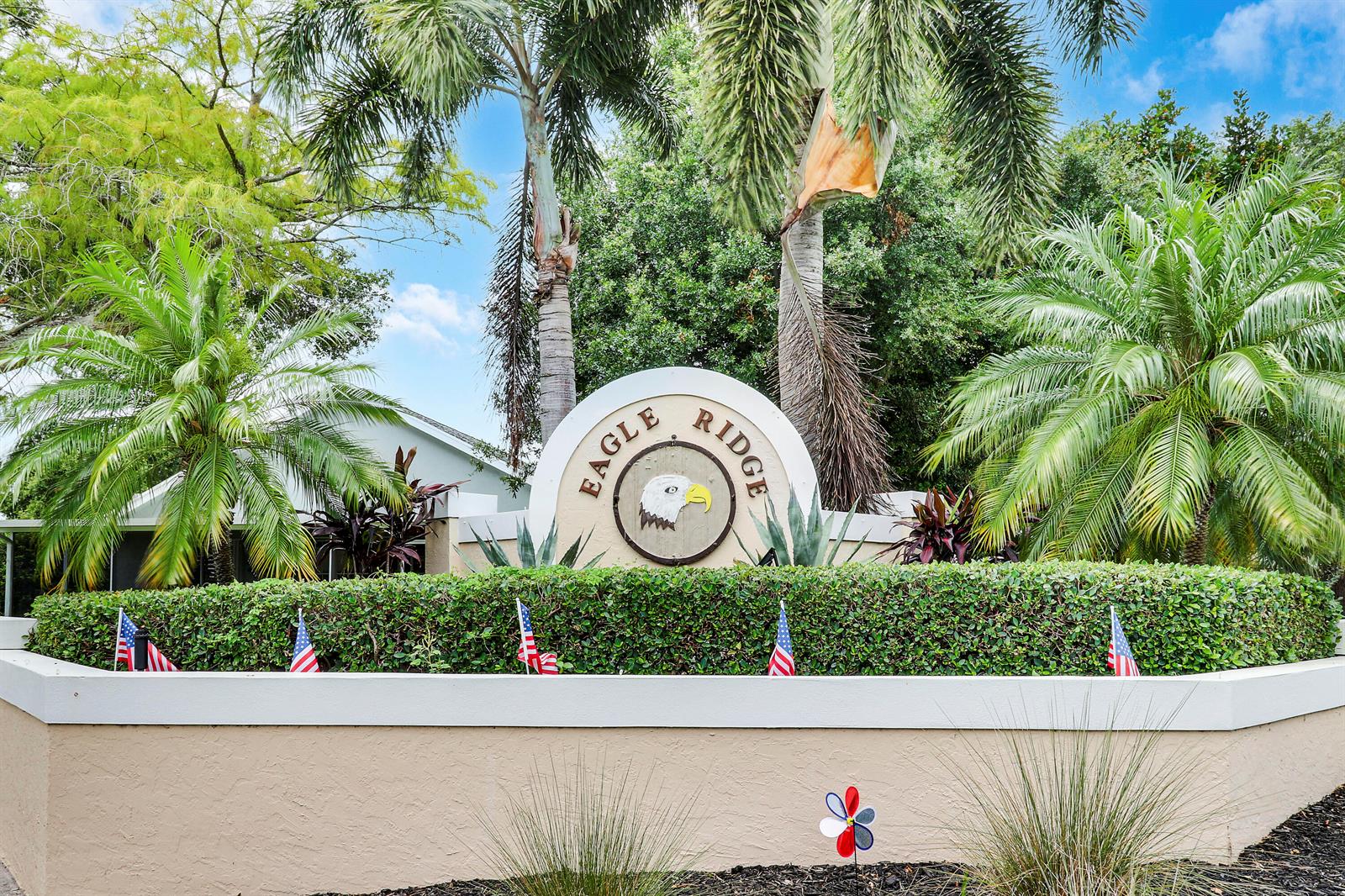 A circular sign with an eagle logo sits behind a hedge decorated with small flags — 234 Moccasin Trail W, Jupiter FL 33458, JUPITER, FL