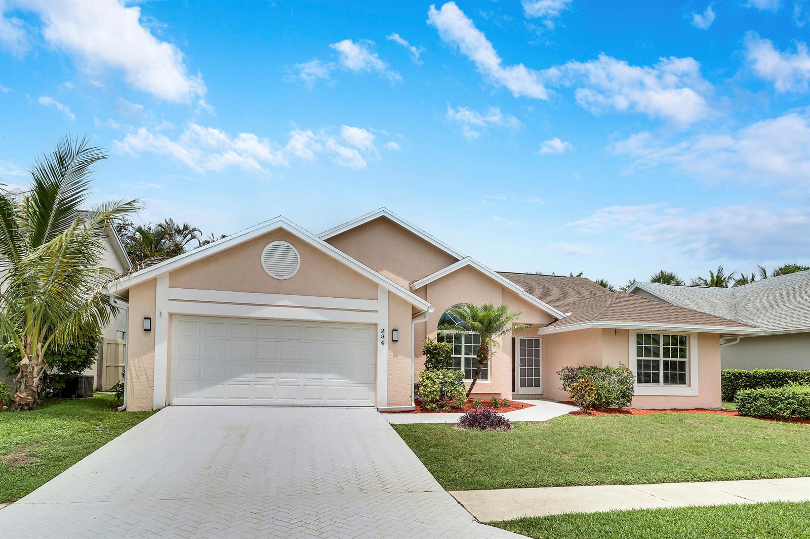 A single-story house with a beige stucco exterior, a two-car garage, and a paved driveway — 234 Moccasin Trail W, Jupiter FL 33458, JUPITER, FL