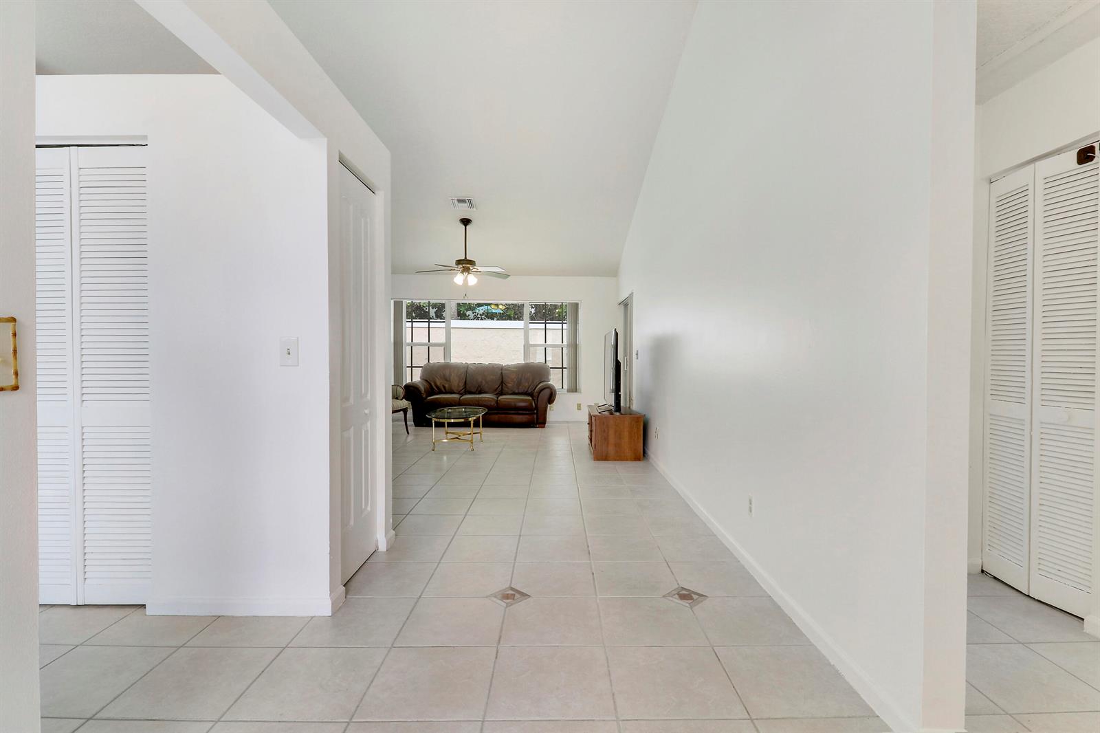 A bright living room features white walls, tiled floors, a vaulted ceiling, and a ceiling fan — 234 Moccasin Trail W, Jupiter FL 33458, JUPITER, FL