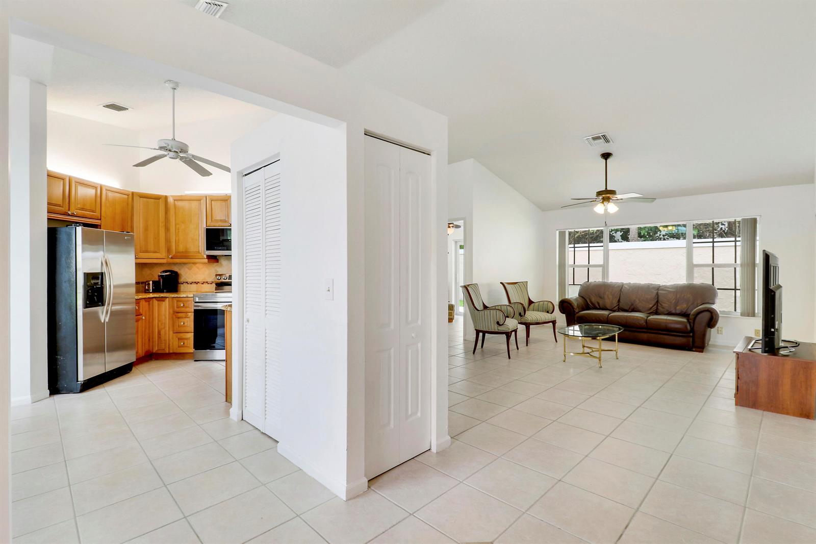 An open-concept living room with tile flooring leads into a kitchen with wood cabinets — 234 Moccasin Trail W, Jupiter FL 33458, JUPITER, FL