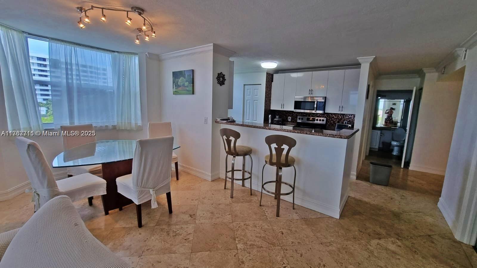 A dining area with a glass table and a kitchen with white cabinets and stools — 3594 S Ocean Blvd # 402, Highland Beach FL 33487, HIGHLAND BEACH, FL