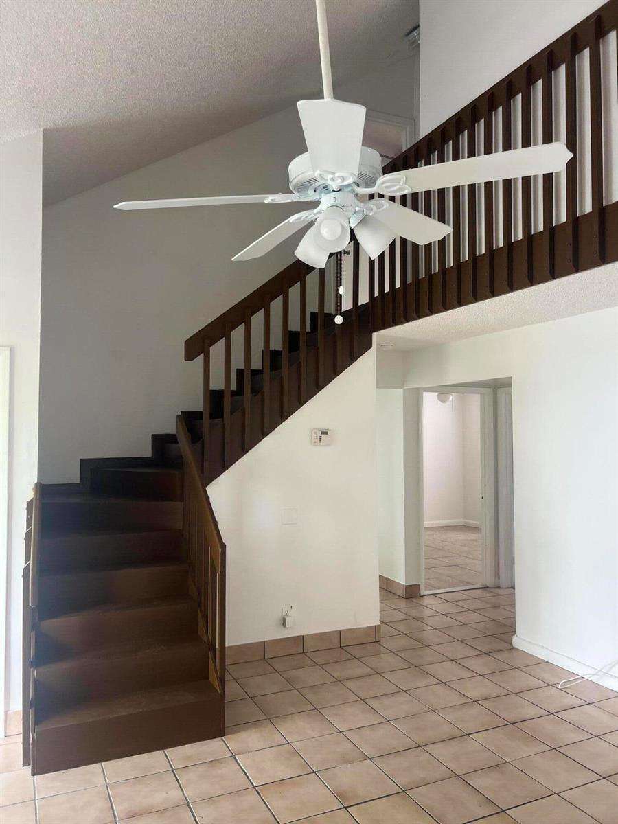 A staircase with dark wood railings leads to a loft above a tiled room — 57 Peachtree Place, Boynton Beach FL 33436, BOYNTON BEACH, FL