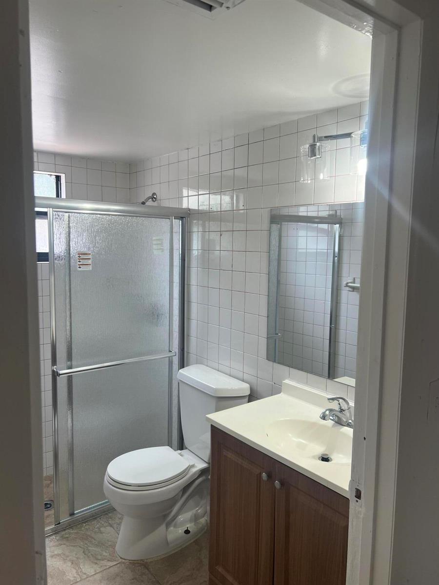 A bathroom features a white toilet, a wood vanity with a sink, and a glass-enclosed shower — 57 Peachtree Place, Boynton Beach FL 33436, BOYNTON BEACH, FL
