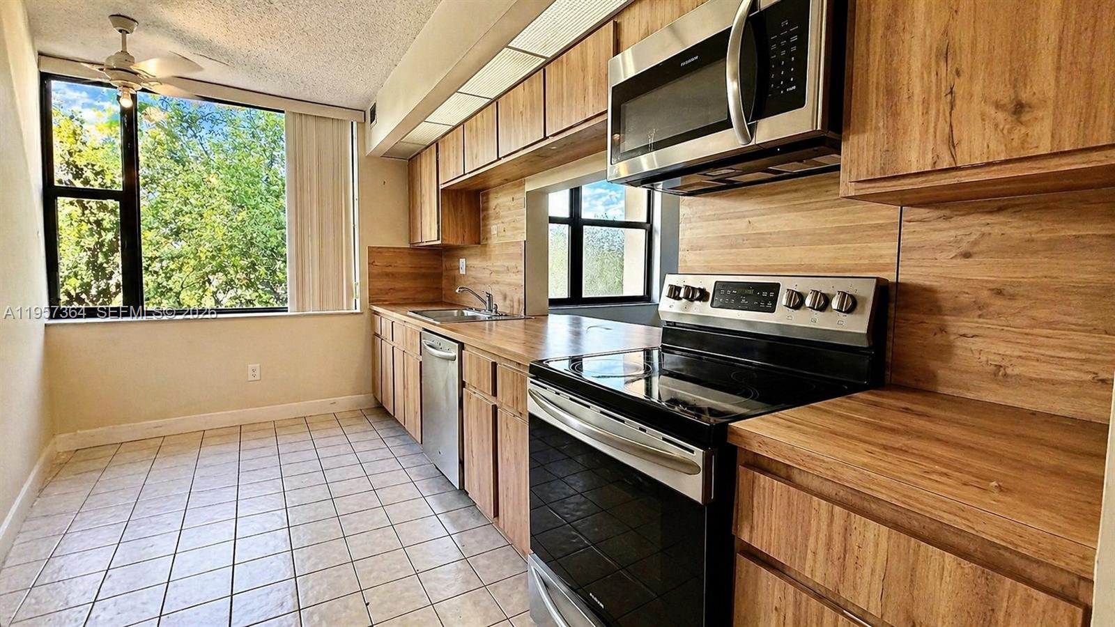 A kitchen features wood-grain cabinets, stainless steel appliances, and tile flooring near a large window — 6800 Cypress Rd # 501, Plantation FL 33317, PLANTATION, FL