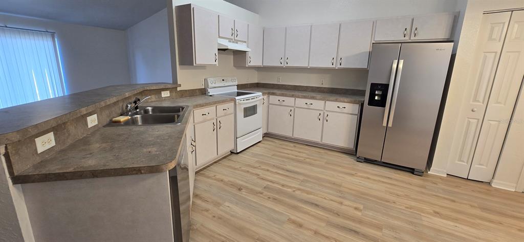 A kitchen features white cabinets, laminate countertops, a stainless steel refrigerator, and light wood flooring — 6875 SE 52ND STREET, OCALA, FL