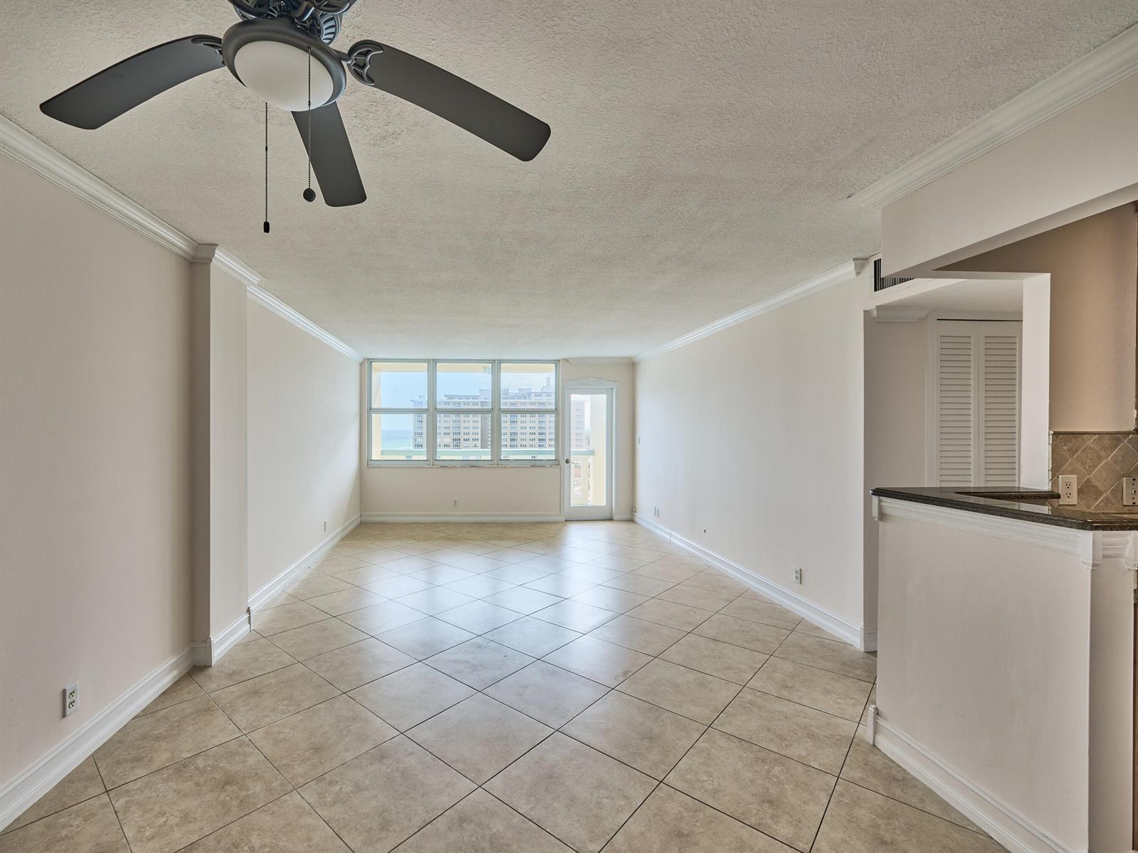 An empty living area features beige tile flooring, a ceiling fan, and a balcony door — 305 N Pompano Beach Boulevard # 1204, Pompano Beach FL 33062, POMPANO BEACH, FL