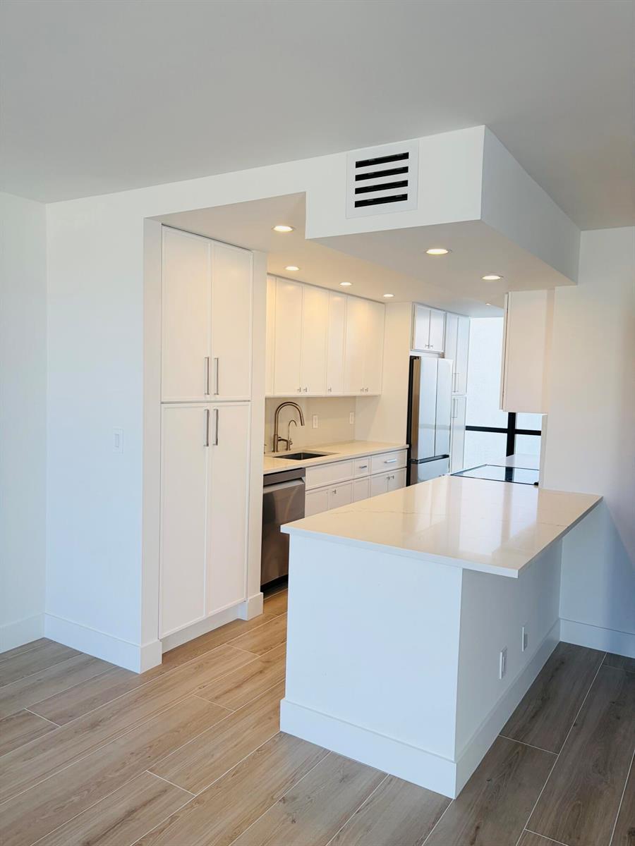A modern white kitchen features a central island, stainless steel appliances, and light wood flooring — 2404 Bridgewood Drive, Boca Raton FL 33434, BOCA RATON, FL