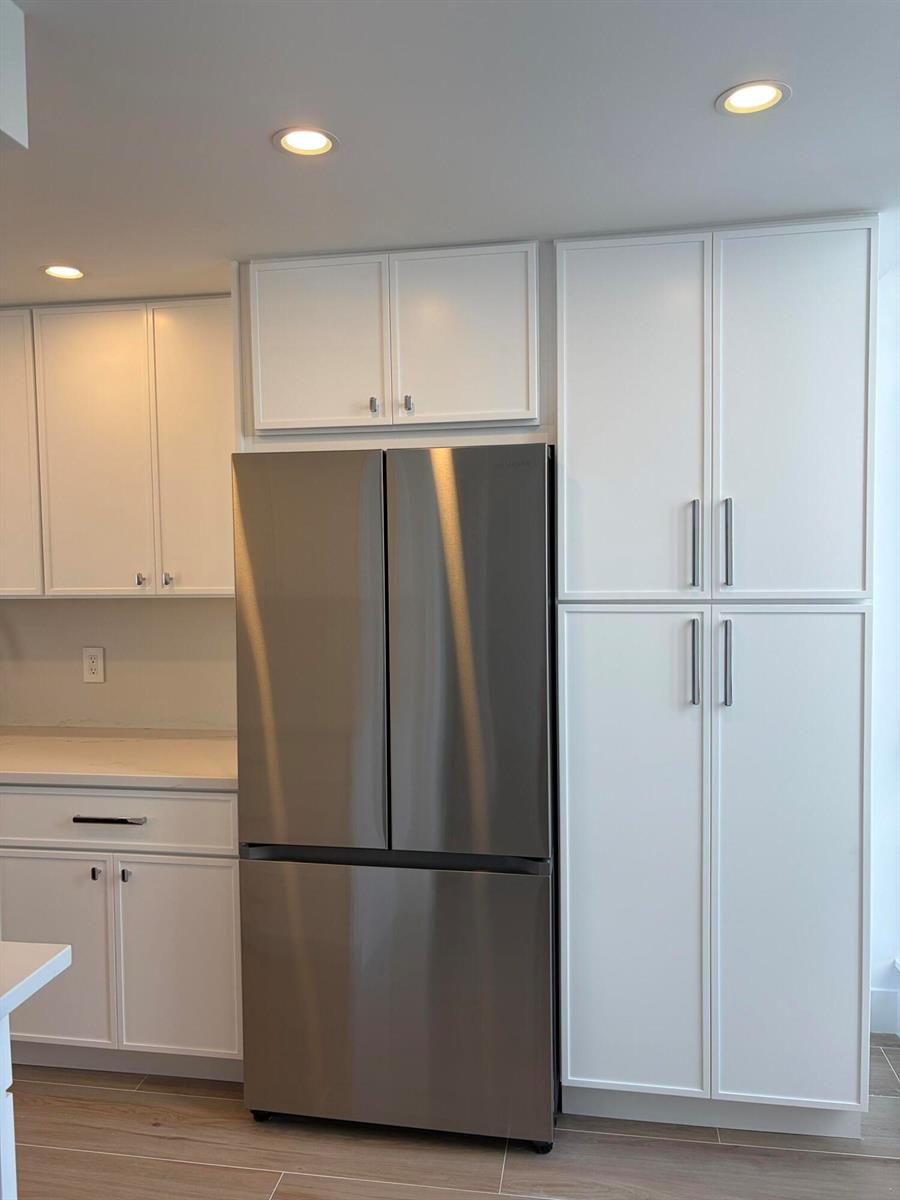 A kitchen features white cabinets, a stainless steel refrigerator, and light-colored wood-look flooring — 2404 Bridgewood Drive, Boca Raton FL 33434, BOCA RATON, FL