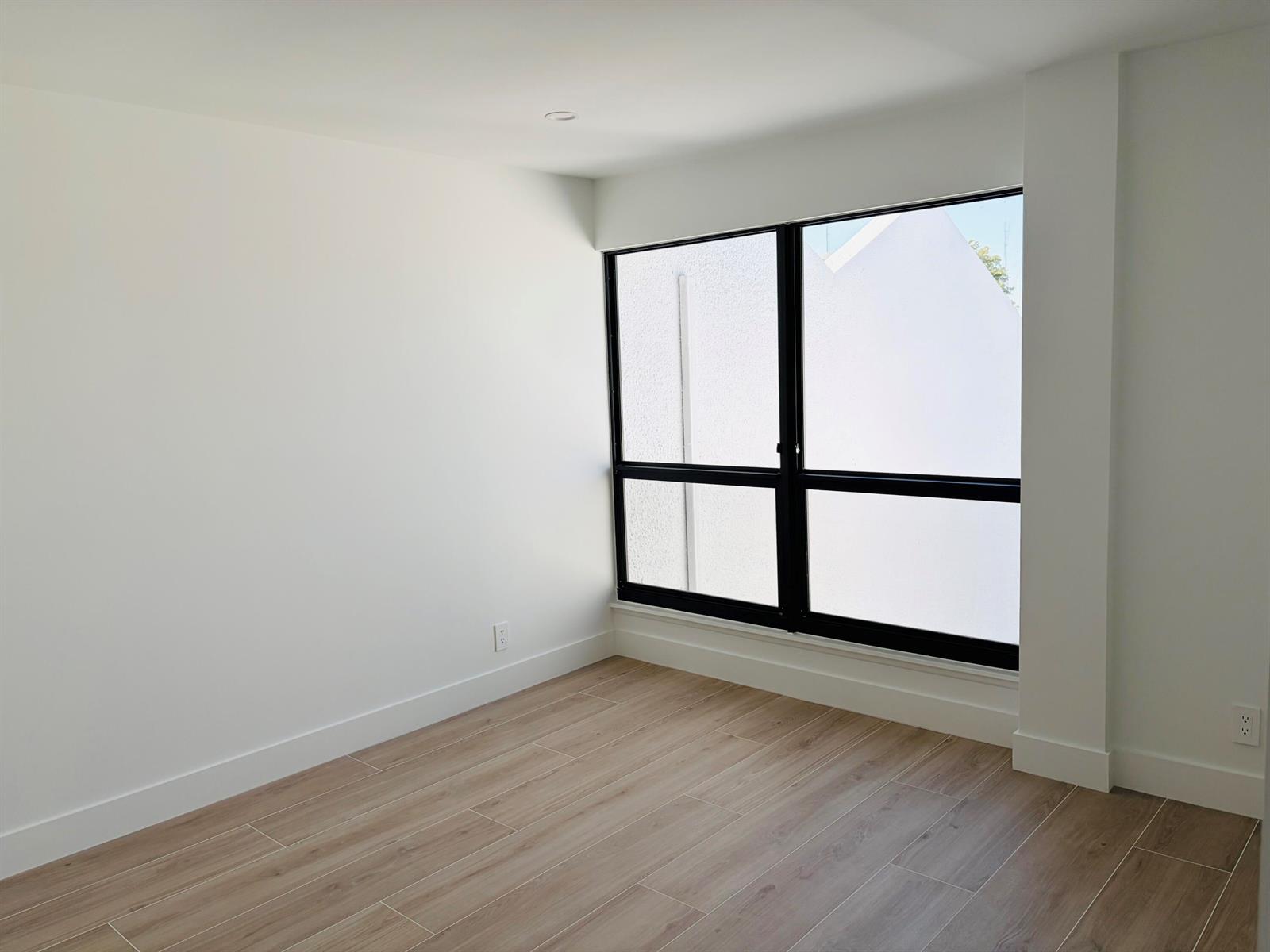 An empty room with white walls, wood-look tile flooring, and a large black-framed window — 2404 Bridgewood Drive, Boca Raton FL 33434, BOCA RATON, FL
