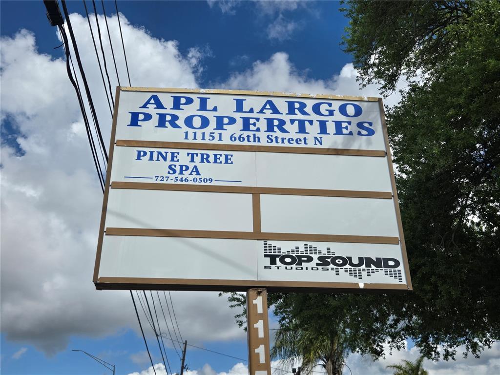 A large outdoor commercial sign displays the names of multiple businesses against a blue sky — 11151 66TH STREET, LARGO, FL