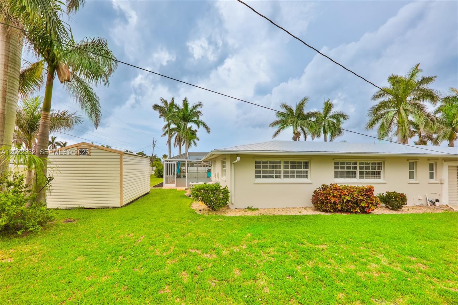 A beige house with a metal roof and a detached shed sits on a lawn — 450 bayshore dr, Cape Coral FL 33904, CAPE CORAL, FL