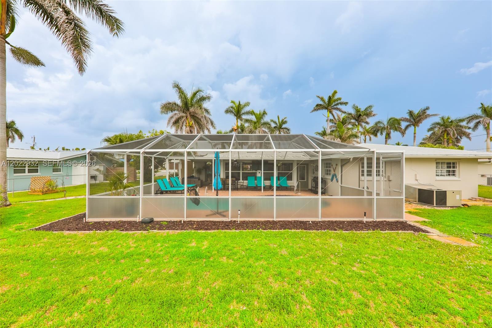 A backyard view of a house with a screened-in pool enclosure and palm trees — 450 bayshore dr, Cape Coral FL 33904, CAPE CORAL, FL