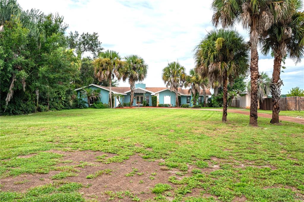 A teal, single-story house sits behind a large, grassy lawn with several palm trees — 589 THORNBURG ROAD, BABSON PARK, FL