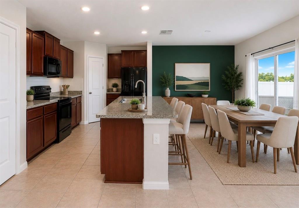 A kitchen with dark wood cabinets, granite countertops, and an island next to a dining area — 17014 YELLOW PINE STREET, WIMAUMA, FL