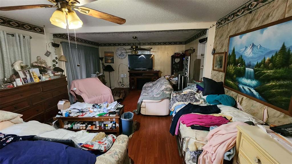 A cluttered living room features wood-look flooring, a ceiling fan, and a large landscape painting — 14451 SE 45TH COURT, SUMMERFIELD, FL
