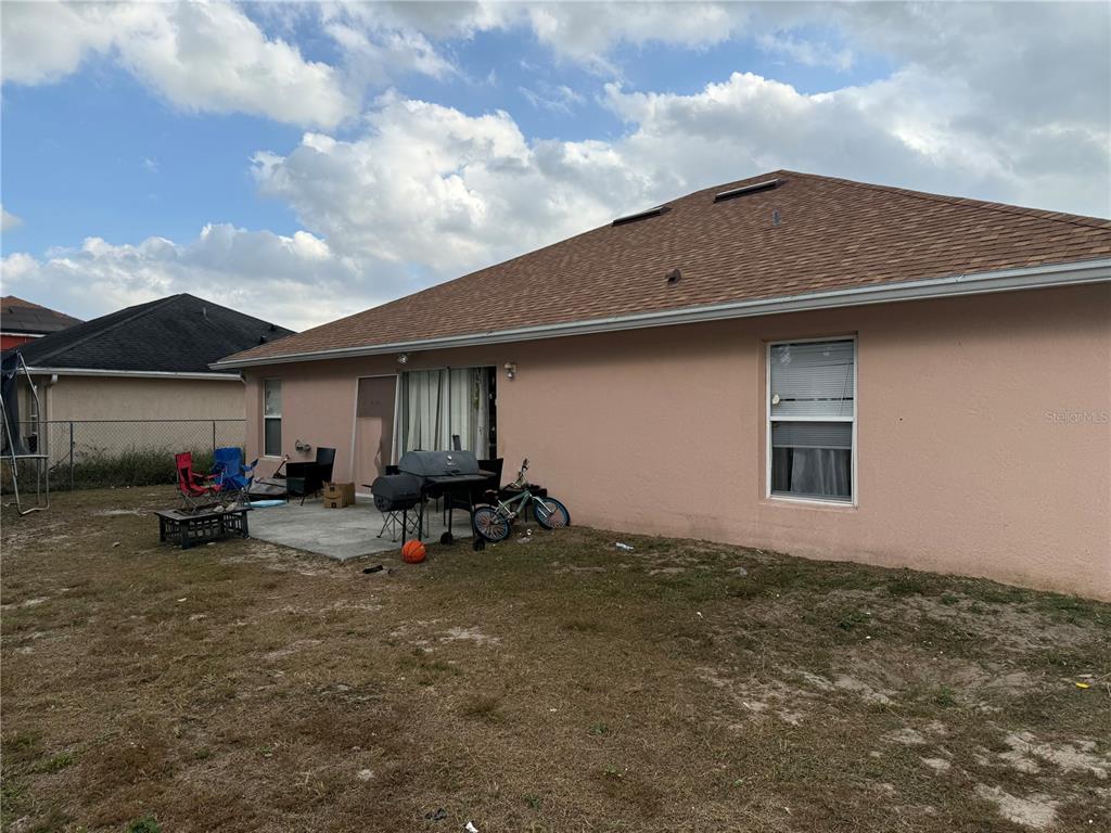 The exterior of a peach-colored house features a concrete patio, a grill, and a yard — 1158 SAINT TROPEZ COURT, KISSIMMEE, FL