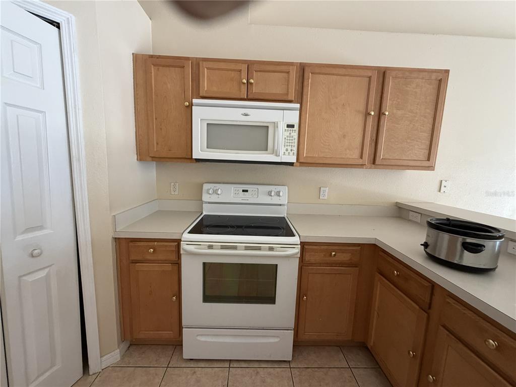 A kitchen features light wood cabinets, white appliances, and beige countertops — 1158 SAINT TROPEZ COURT, KISSIMMEE, FL