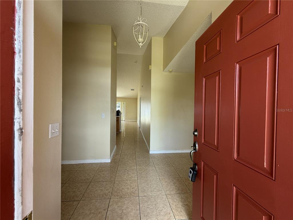 An open front door reveals a tiled entryway leading to a long hallway — 1158 SAINT TROPEZ COURT, KISSIMMEE, FL