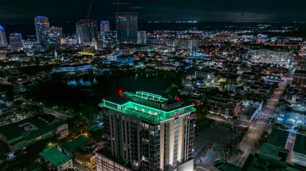 An aerial night view of a high-rise building with a glowing green rooftop pool area — 777 3RD AVENUE N UNIT 1605, ST PETERSBURG, FL