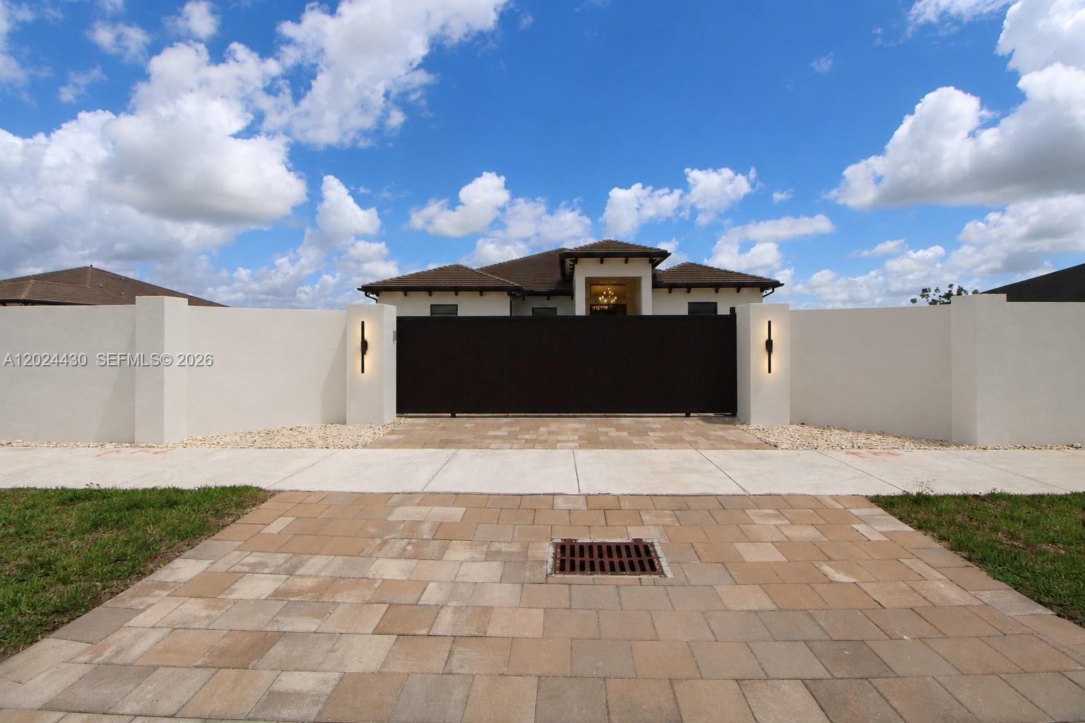 A gated entrance with a paved driveway leads to a single-story house with white walls — 18321 SW 224th St # 0, Miami FL 33170, MIAMI, FL