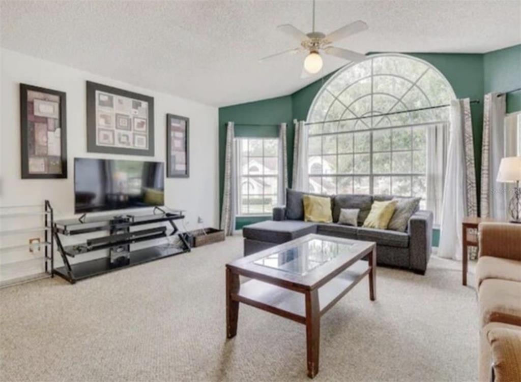 A living room features a large arched window, gray sectional sofa, and a glass-topped coffee table — 5004 LAGUNA BAY CIRCLE UNIT 54, KISSIMMEE, FL