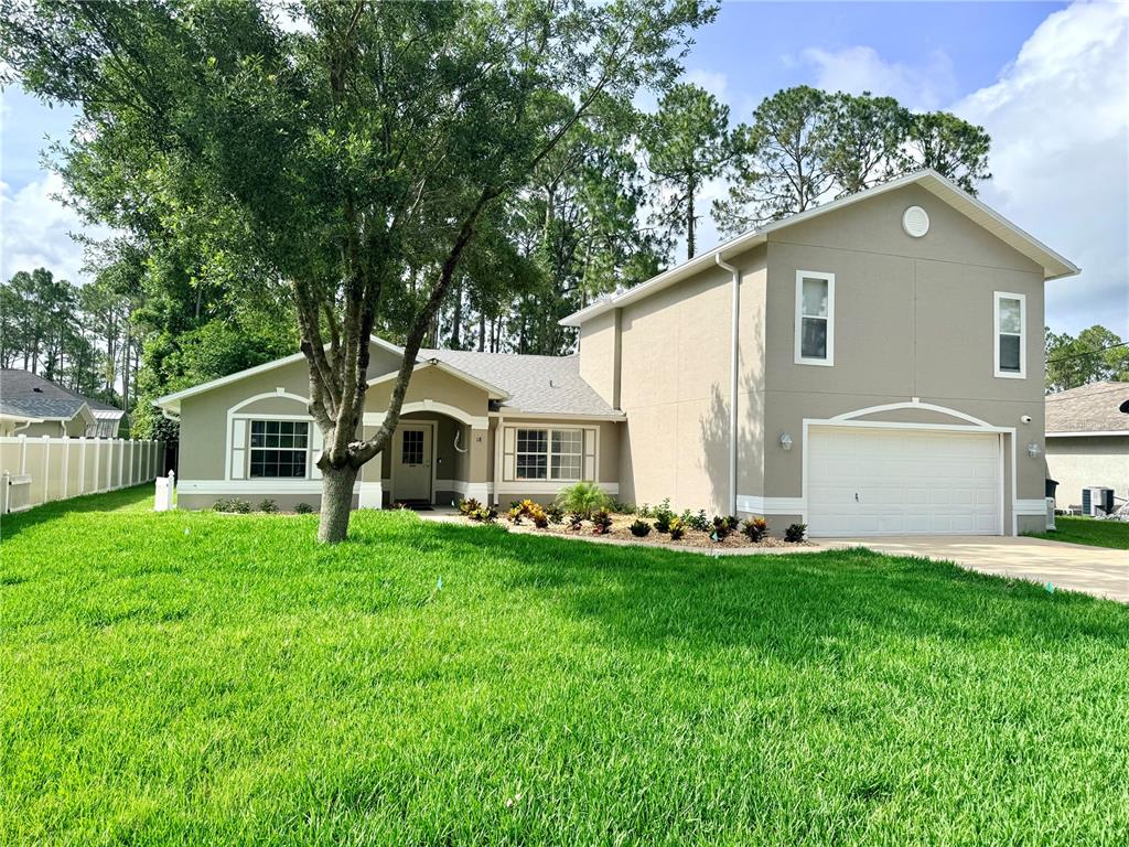 A two-story house with a tan exterior, a two-car garage, and a large front lawn — 18 BURNING VIEW LANE, PALM COAST, FL