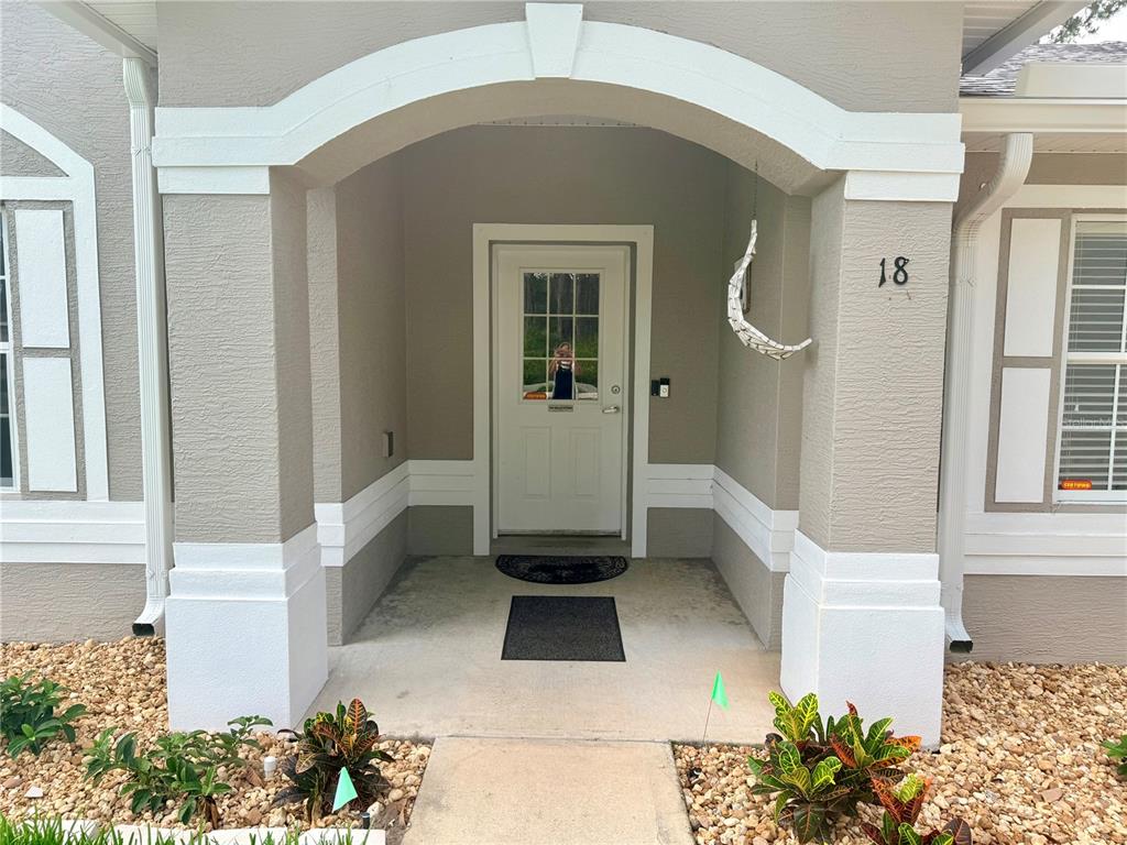 The front entrance of a house features a white door, arched porch, and rock landscaping — 18 BURNING VIEW LANE, PALM COAST, FL