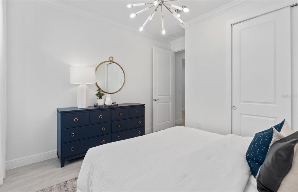 A bedroom features a dark blue dresser, a round mirror, and a modern light fixture — 6807 SUNRISE COVE DRIVE, CLERMONT, FL