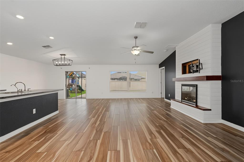 A living room features wood-look tile flooring, a white shiplap fireplace, and an adjacent kitchen — 6317 SPIDER LILY WAY, NEW PORT RICHEY, FL