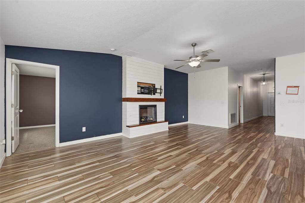 A living room features wood-look tile flooring, a white shiplap fireplace, and dark blue accent walls — 6317 SPIDER LILY WAY, NEW PORT RICHEY, FL