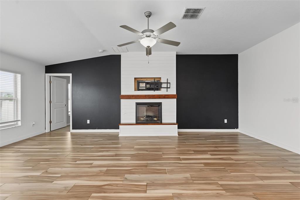 A living room features wood-look tile flooring, a white shiplap fireplace, and black accent walls — 6317 SPIDER LILY WAY, NEW PORT RICHEY, FL