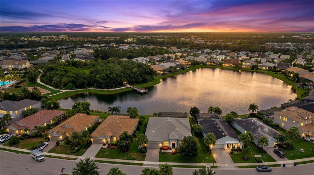 An aerial view of a suburban neighborhood featuring houses surrounding a central lake at sunset — 12105 SEABROOK AVENUE, BRADENTON, FL