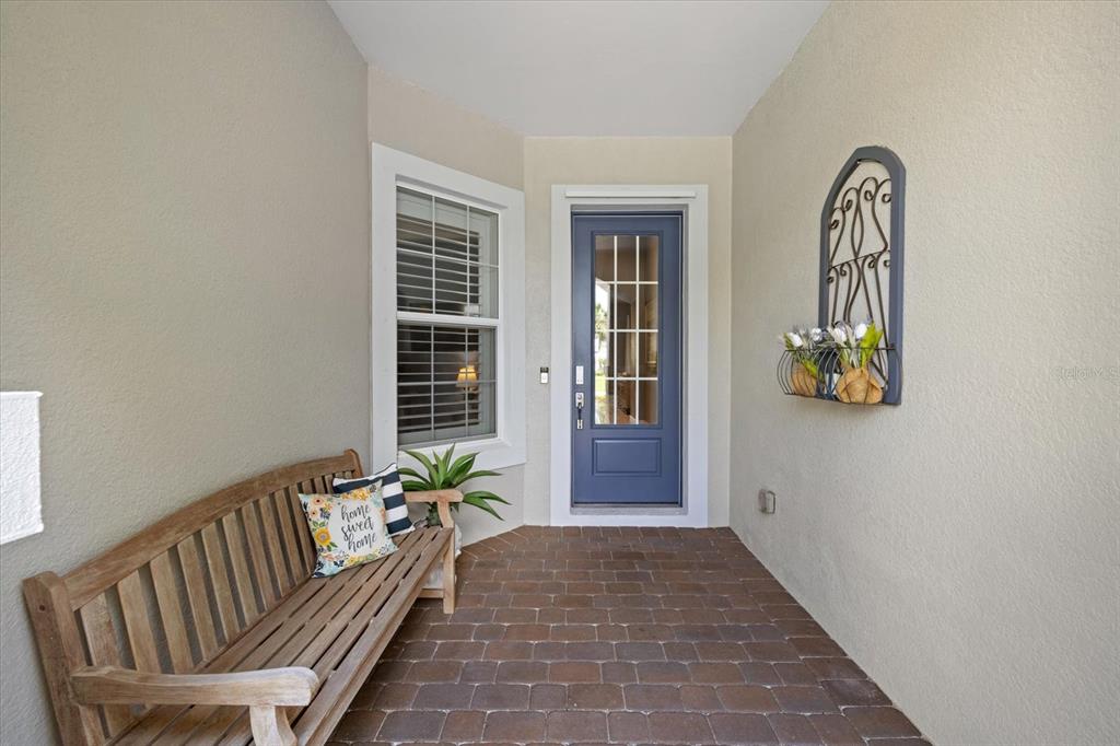 A covered front porch features a wooden bench, a blue front door, and brick pavers — 12105 SEABROOK AVENUE, BRADENTON, FL