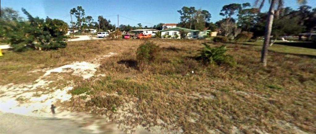 A vacant, grassy lot with sparse vegetation and sandy patches sits in a residential neighborhood — 215 LAVERNE STREET, PUNTA GORDA, FL