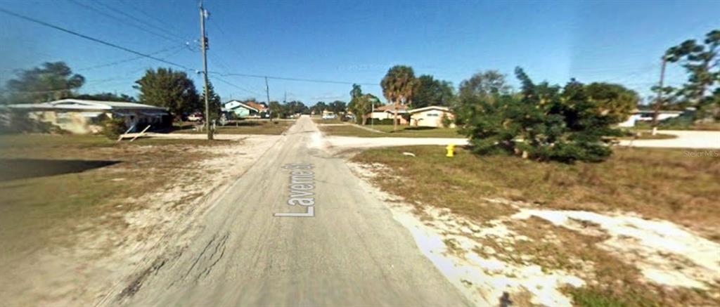 This street-level view shows a paved road with sandy shoulders and surrounding residential houses — 215 LAVERNE STREET, PUNTA GORDA, FL