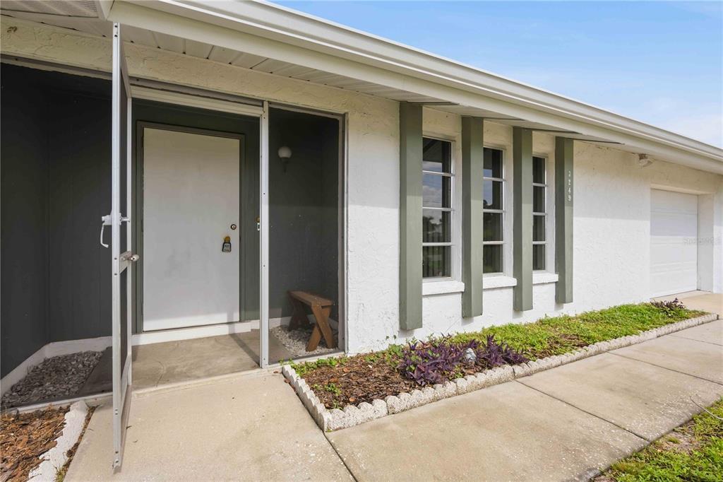 A white house exterior features a screened entryway, vertical window accents, and a concrete walkway — 3249 SUNRISE TRAIL, PORT CHARLOTTE, FL