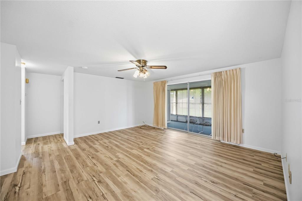 An empty living room with wood-look flooring, a ceiling fan, and sliding glass doors — 3249 SUNRISE TRAIL, PORT CHARLOTTE, FL