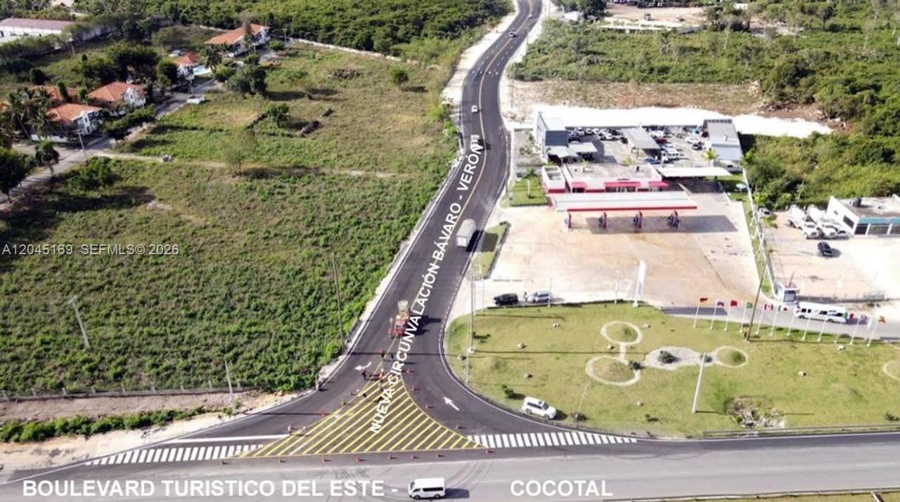 An aerial view shows a road intersection with a gas station and surrounding undeveloped land — veron bavaro, FL