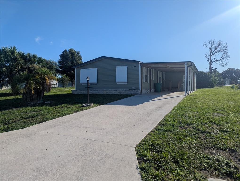 A single-story manufactured home features a concrete driveway, a carport, and white window shutters — 1385 KISKADEE DRIVE, ENGLEWOOD, FL