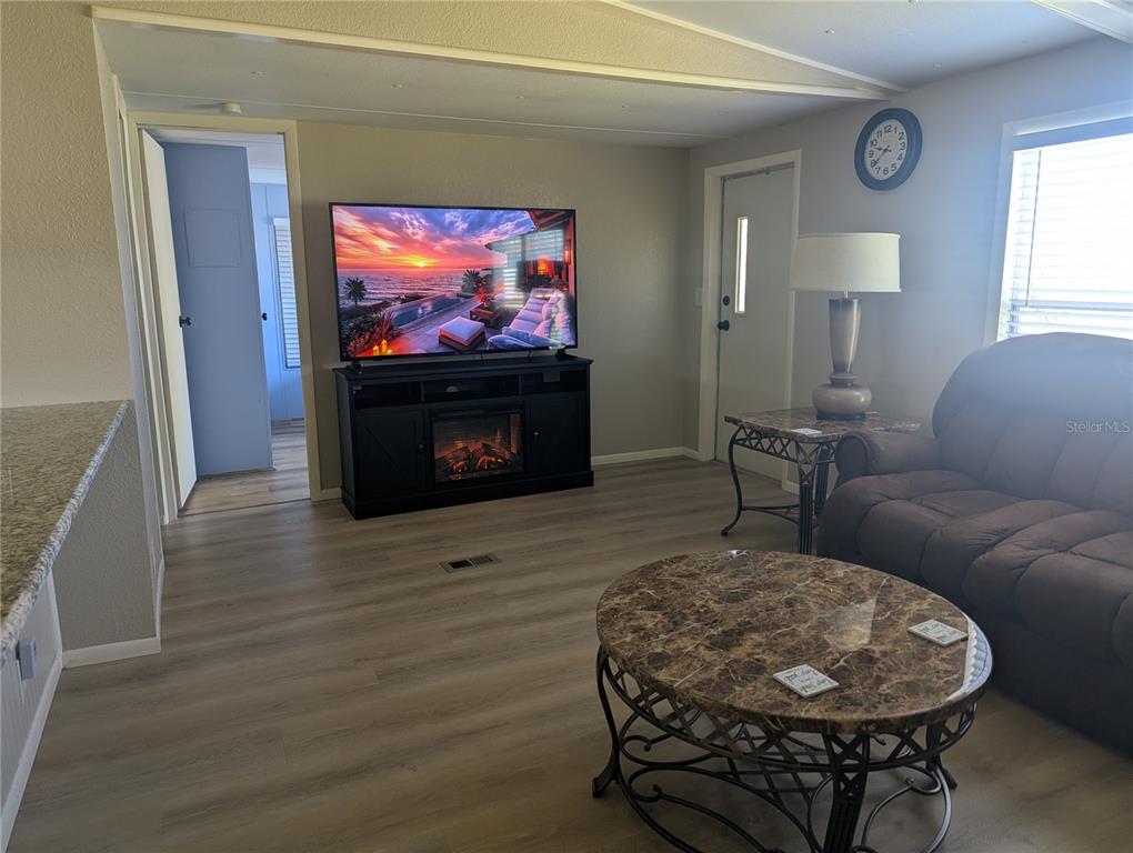 A living room features light wood-look flooring, a television on a fireplace console, and furniture — 1385 KISKADEE DRIVE, ENGLEWOOD, FL