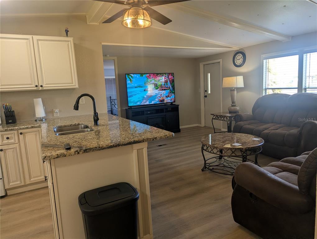 An open-concept kitchen with granite countertops overlooks a living area featuring a television and sofa — 1385 KISKADEE DRIVE, ENGLEWOOD, FL