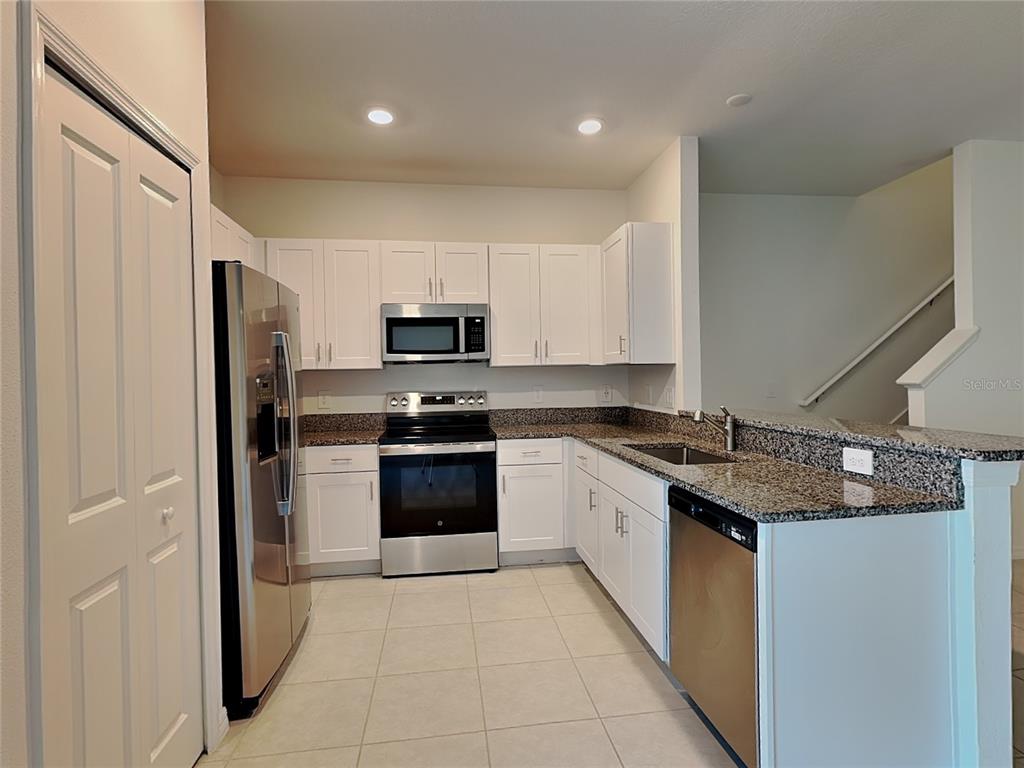 A kitchen features white cabinets, stainless steel appliances, and granite countertops with tile flooring — 9207 BONITA MAR DRIVE, PARRISH, FL