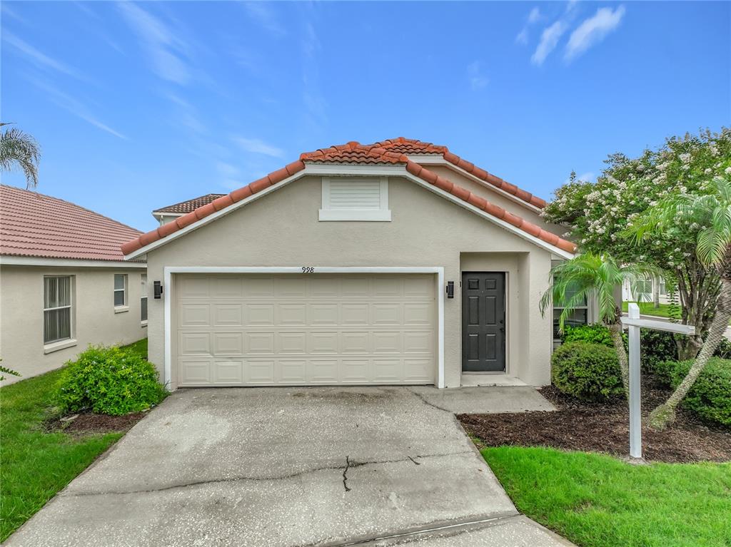 A single-story house exterior features a beige stucco facade, a two-car garage, and tiled roof — 998 WHITE SPRINGS LANE, WINTER SPRINGS, FL