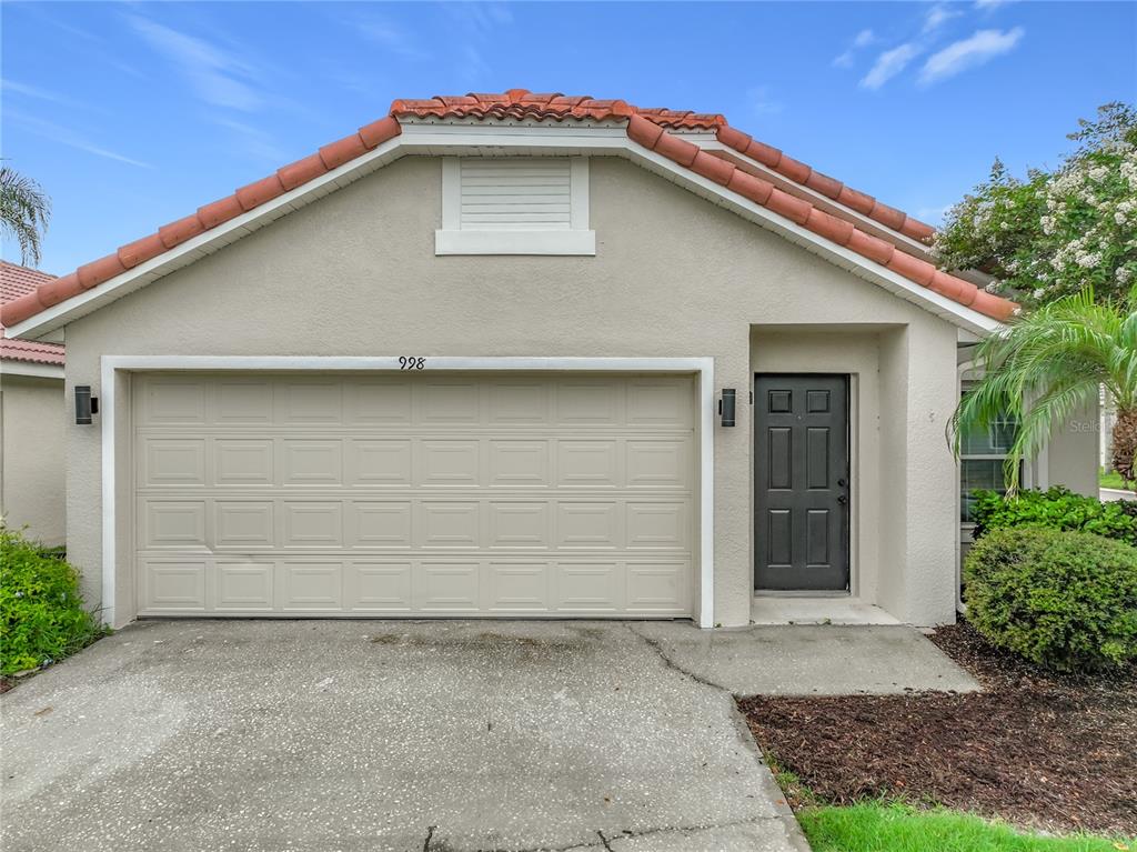 A beige house exterior features a two-car garage, a dark front door, and a tiled roof — 998 WHITE SPRINGS LANE, WINTER SPRINGS, FL
