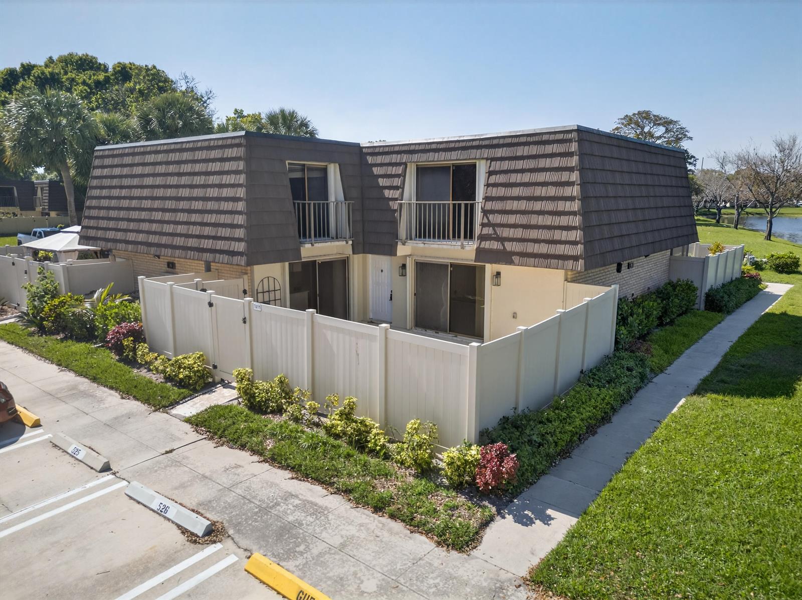 An exterior view of a two-story townhouse with a brown mansard roof and private fenced patio — 7811 78th Way, West Palm Beach FL 33407, WEST PALM BEACH, FL