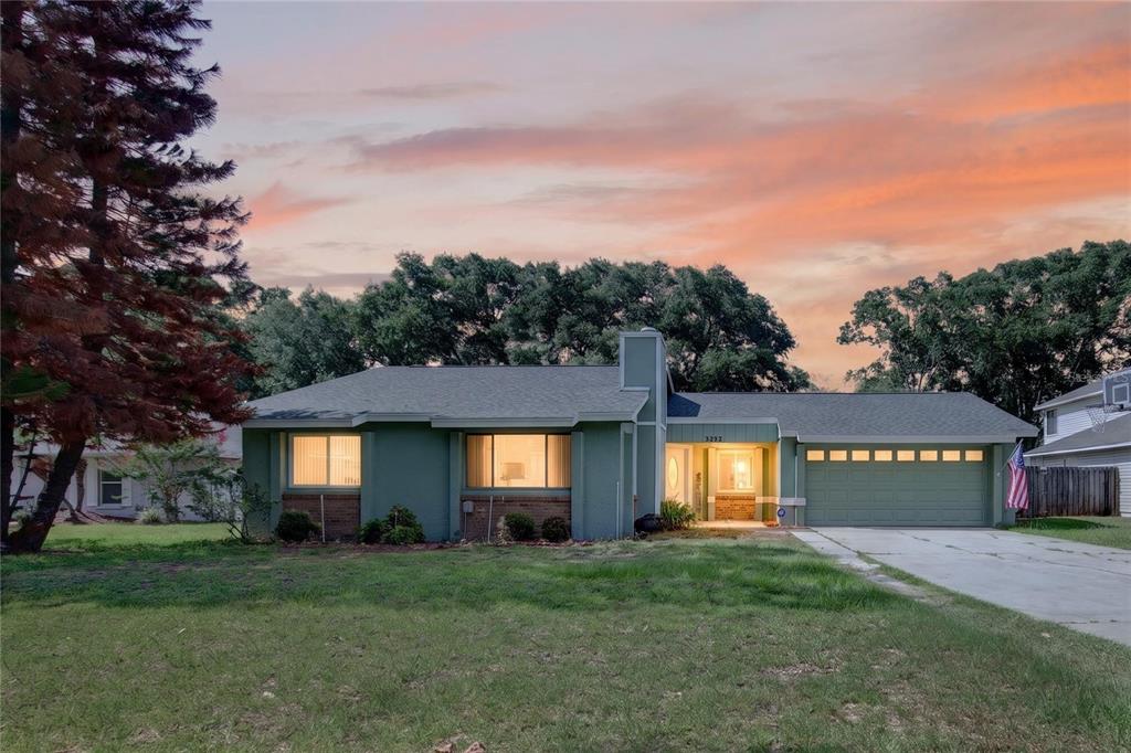 A single-story green house with a two-car garage and a large front lawn at sunset — 3303 FOXBORO COURT, MOUNT DORA, FL