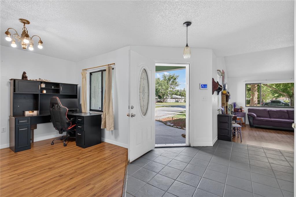 An entryway with gray tile flooring transitions into a wood-floored office area and living room — 3303 FOXBORO COURT, MOUNT DORA, FL