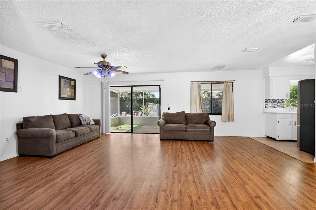 A living room with wood-look flooring, two brown sofas, a ceiling fan, and sliding doors — 3303 FOXBORO COURT, MOUNT DORA, FL